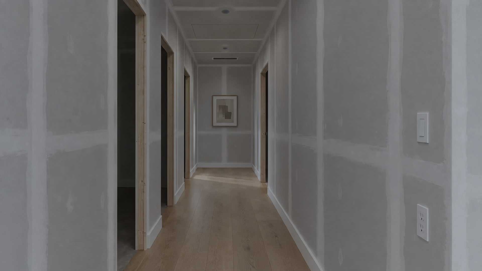 The same hallway before: lights off, bare walls and open doorways