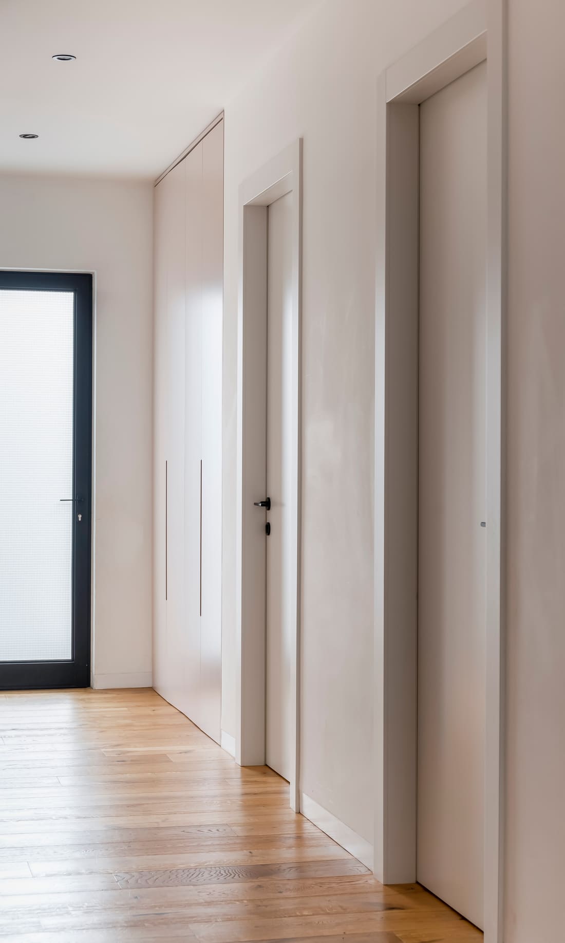 A hallway of white flush interior doors over a wood floor